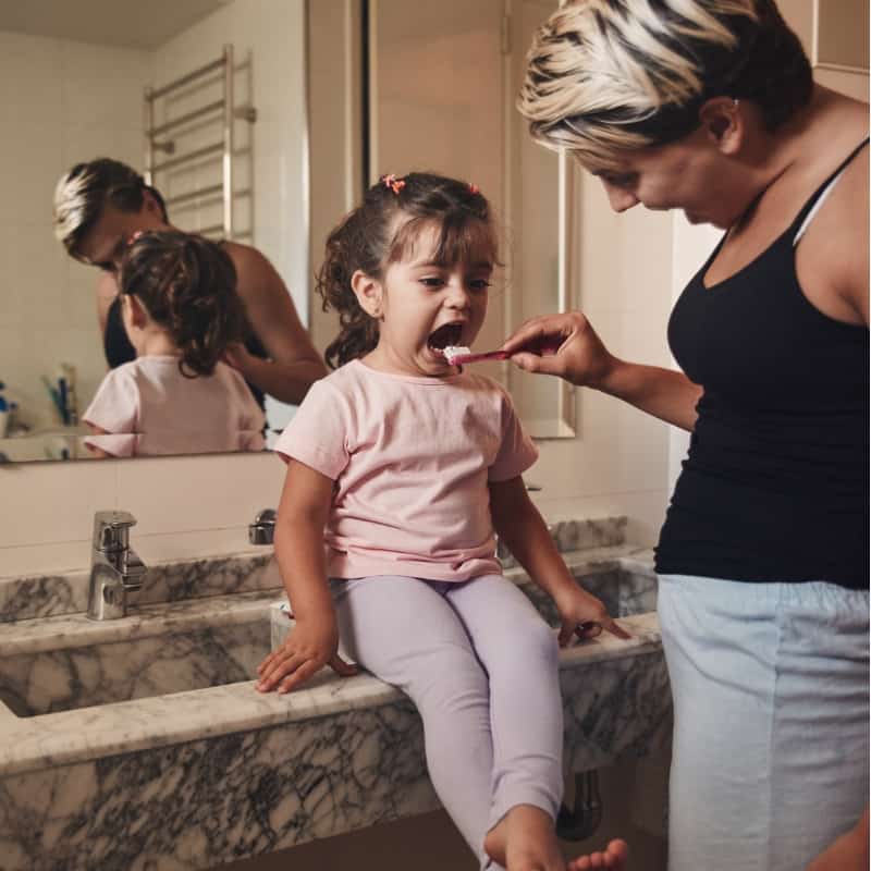 little girl brushing teeth with Mom